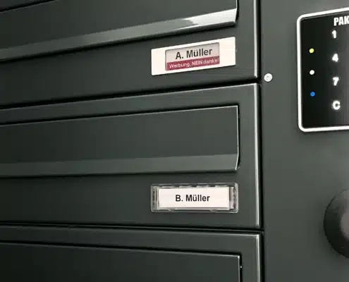 Das Foto zeigt eine dunkelgraue kombinierte Briefkasten- und Paketkastenanlage, bei der die digitalen Namensschildern von PAKETIN nachgerüstet wurden.