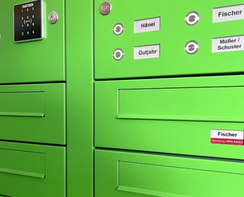 Das Foto zeigt eine grüne kombinierte Briefkasten- und Klingelanlage mit digitalen Namensschildern von PAKETIN.