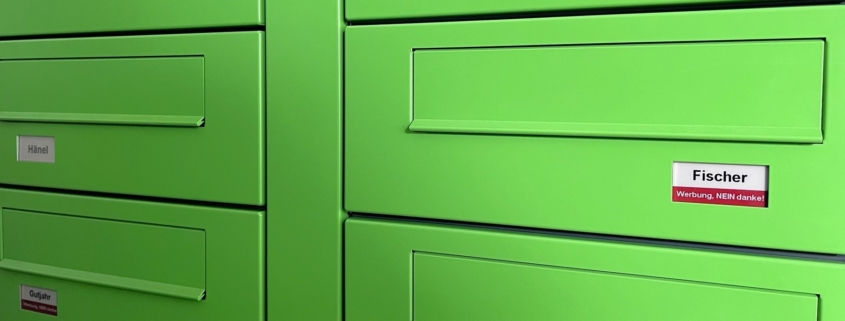 Das Foto zeigt eine grüne kombinierte Briefkasten- und Klingelanlage mit digitalen Namensschildern von PAKETIN.